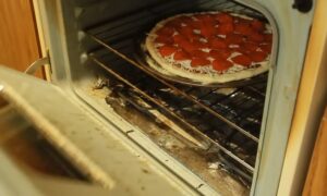 An unbaked pepperoni pizza topped with cheese and pepperoni slices sitting on a rack inside an open oven