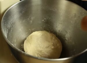 A smooth, kneaded ball of homemade pizza dough inside a stainless steel stand mixer bowl for a pepperoni pizza recipe
